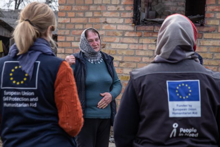 2 aid workers seen from the back talking to a woman outside a house.