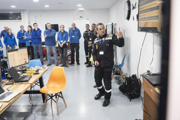 A man wearing a civil protection uniform points to a screen during a presentation.