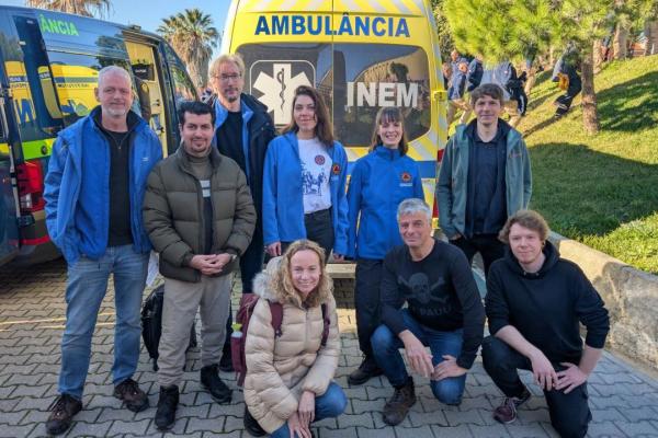 6 people stand in front of an ambulance. 3 kneel on the ground. Some wear blue Union Civil Protection Mechanism jackets.